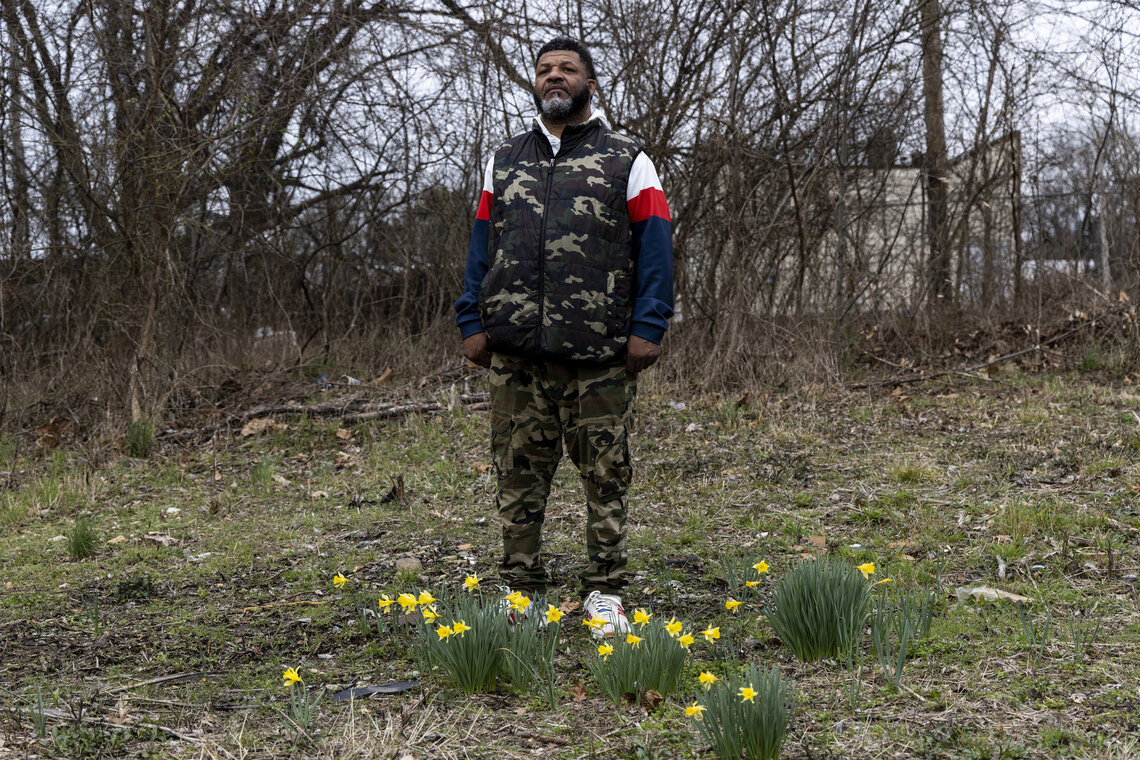 Reginald Monroe, a Black man, stands in a field with flowers blooming at his feet.  