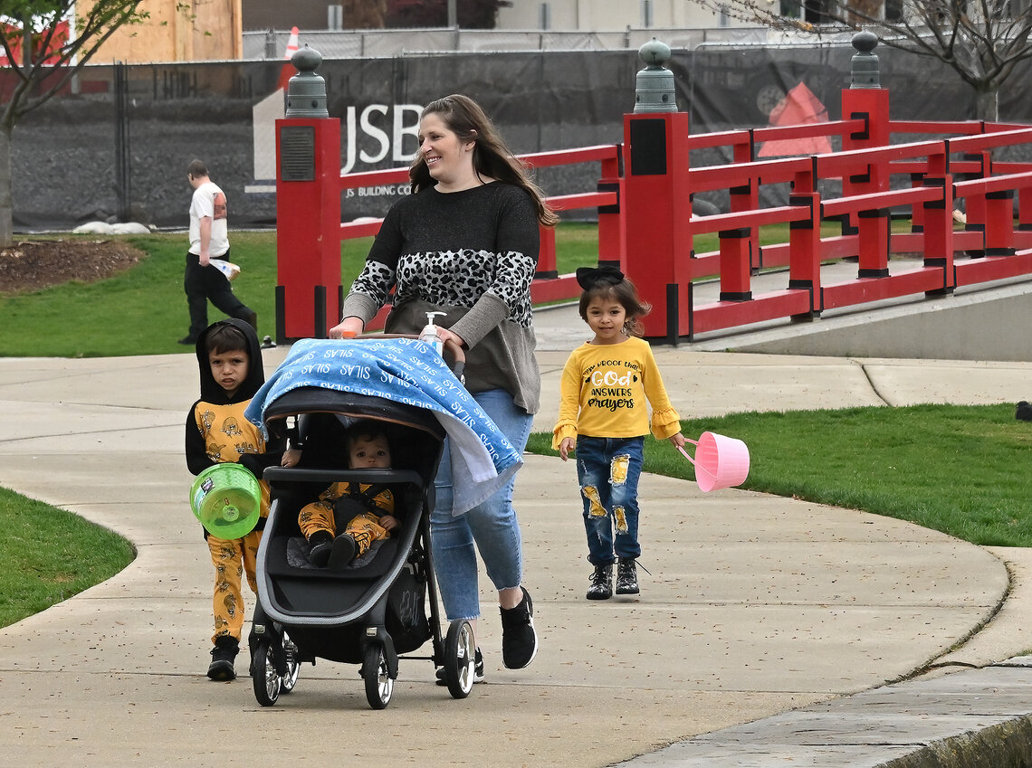 A light skin-toned woman pushes a stroller while   walking through a park with her three children.