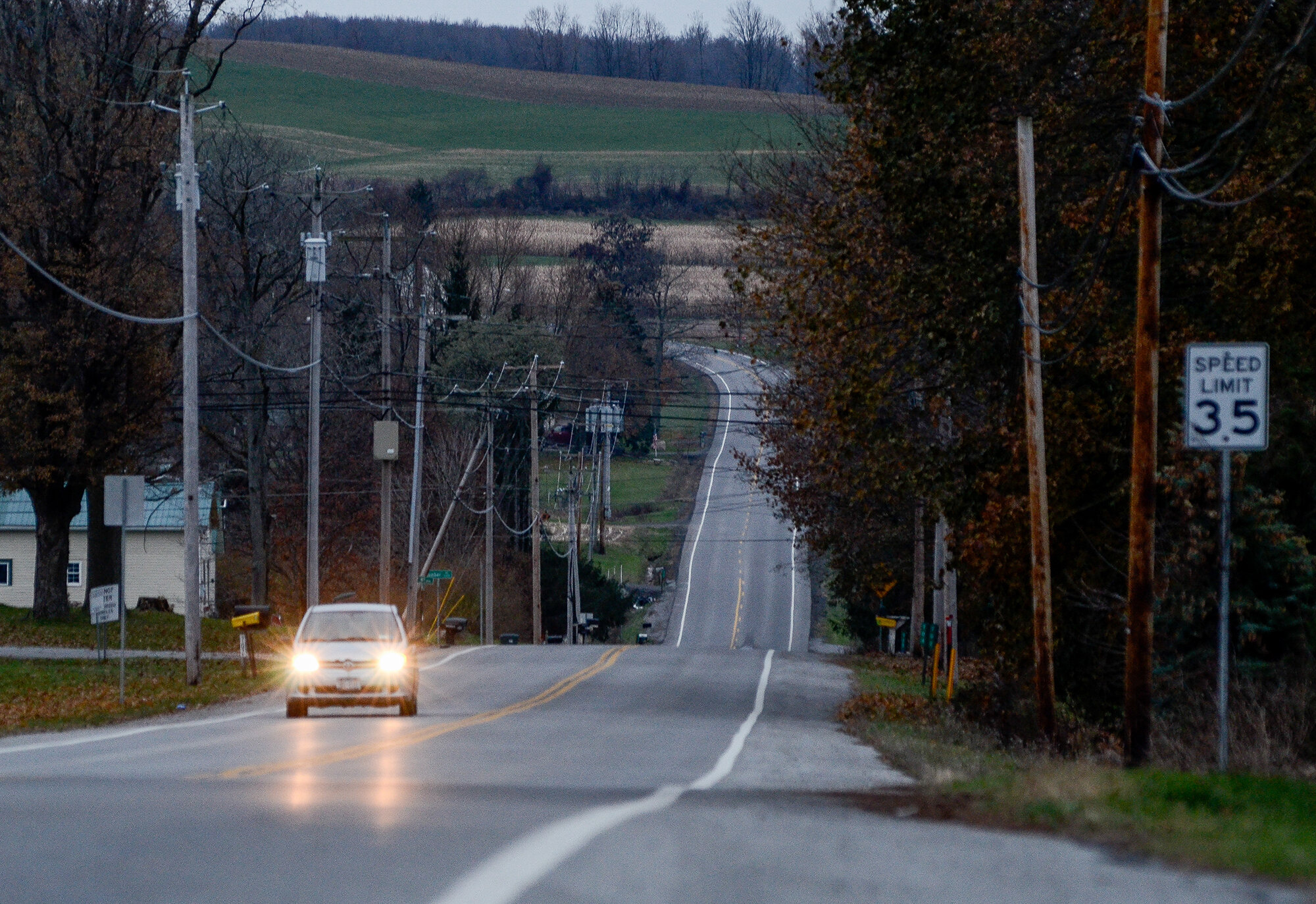 A car with headlights on drives on a road leading off into the distance near Attica Correctional Facility at dusk. 