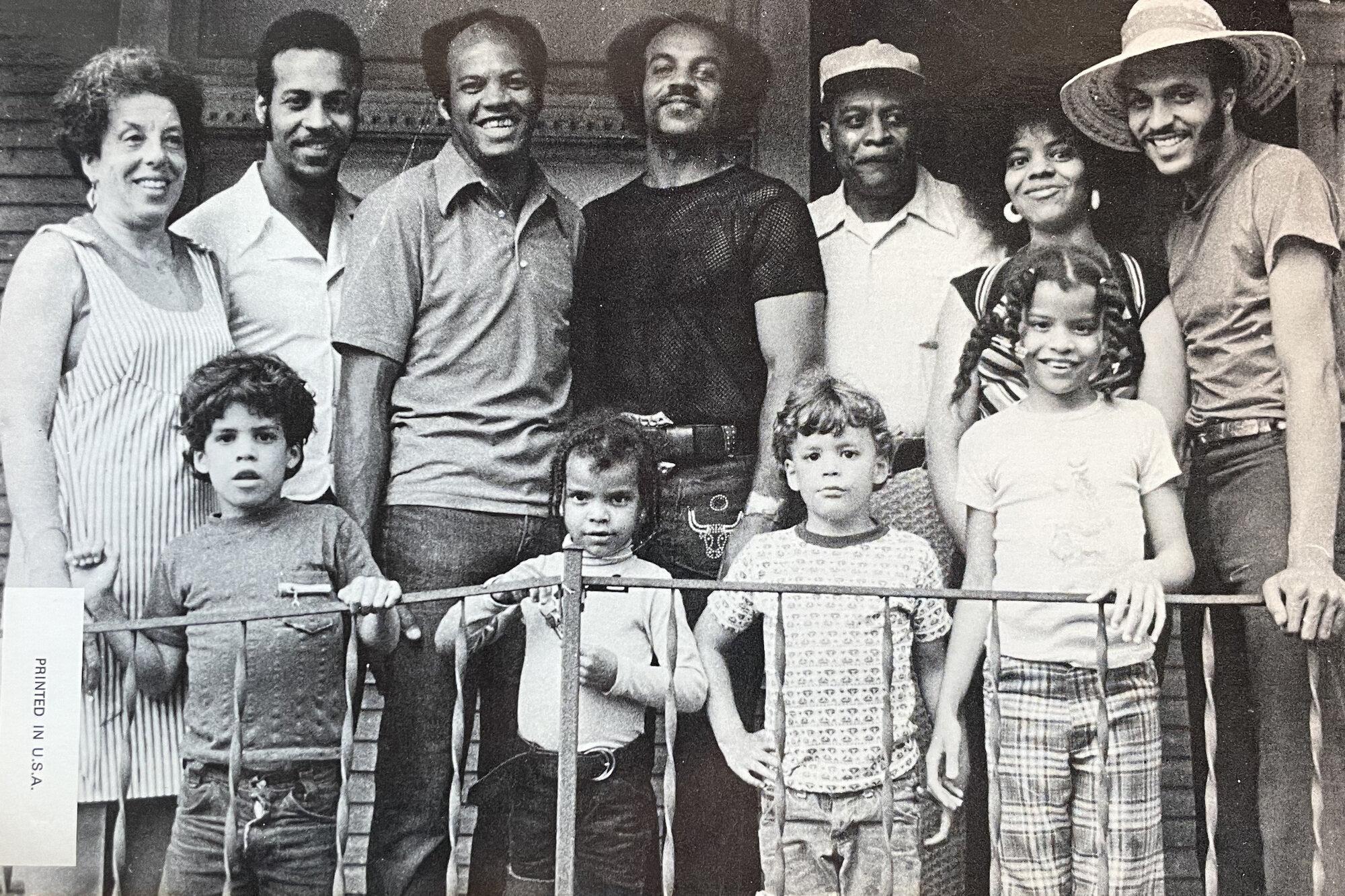 A black and white image shows a group of adults and four children standing and smiling while looking at the camera. 